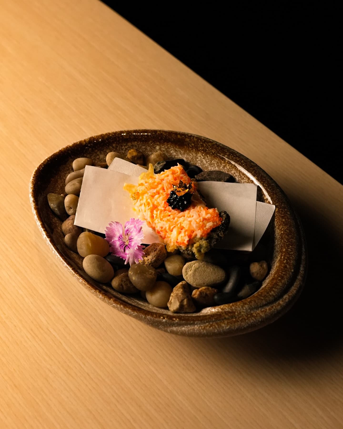 Crab meat with caviar and an edible flower on paper in a stone bowl of pebbles