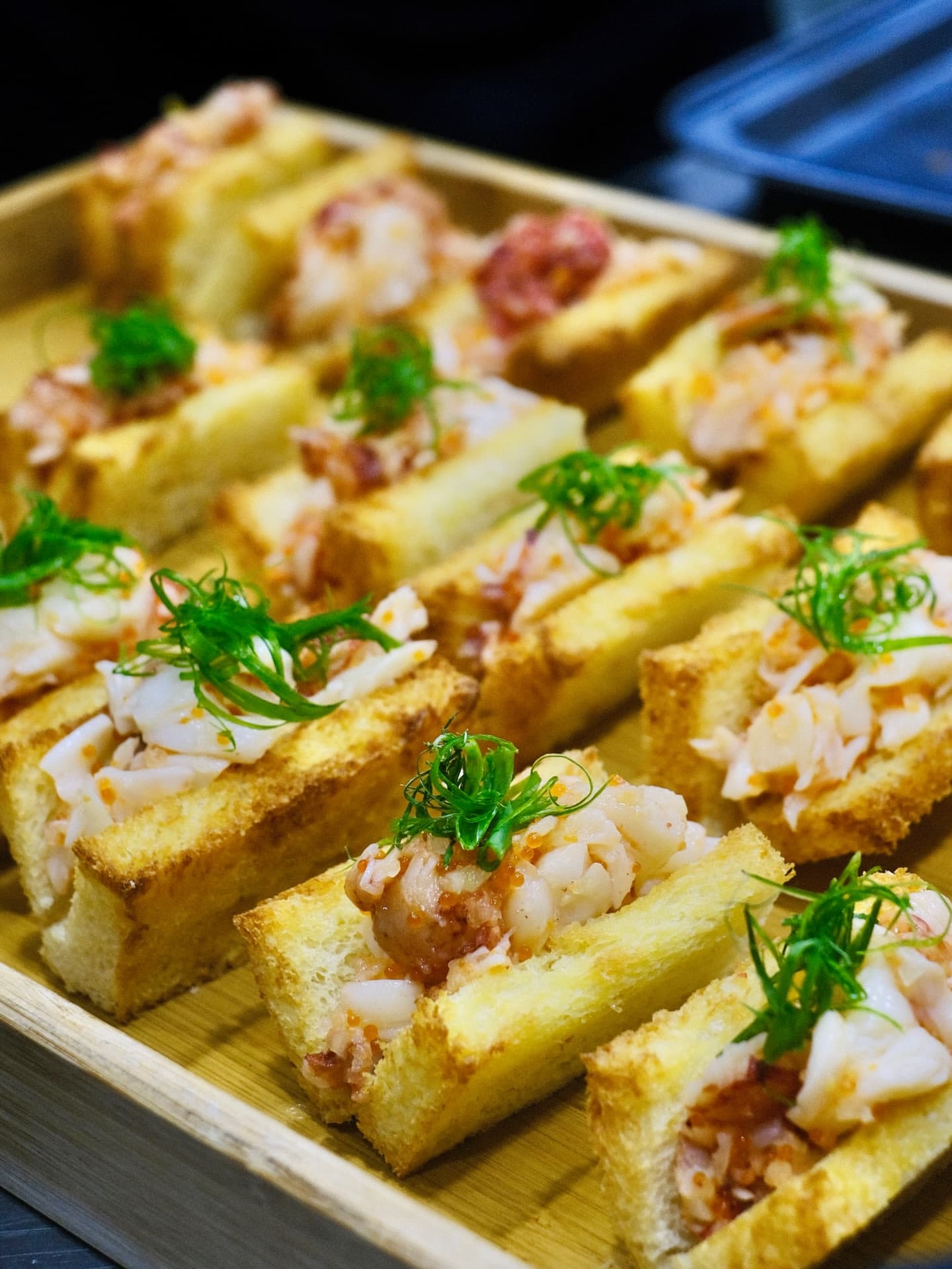 Toast fingers topped with crab and spring onion in a wooden box