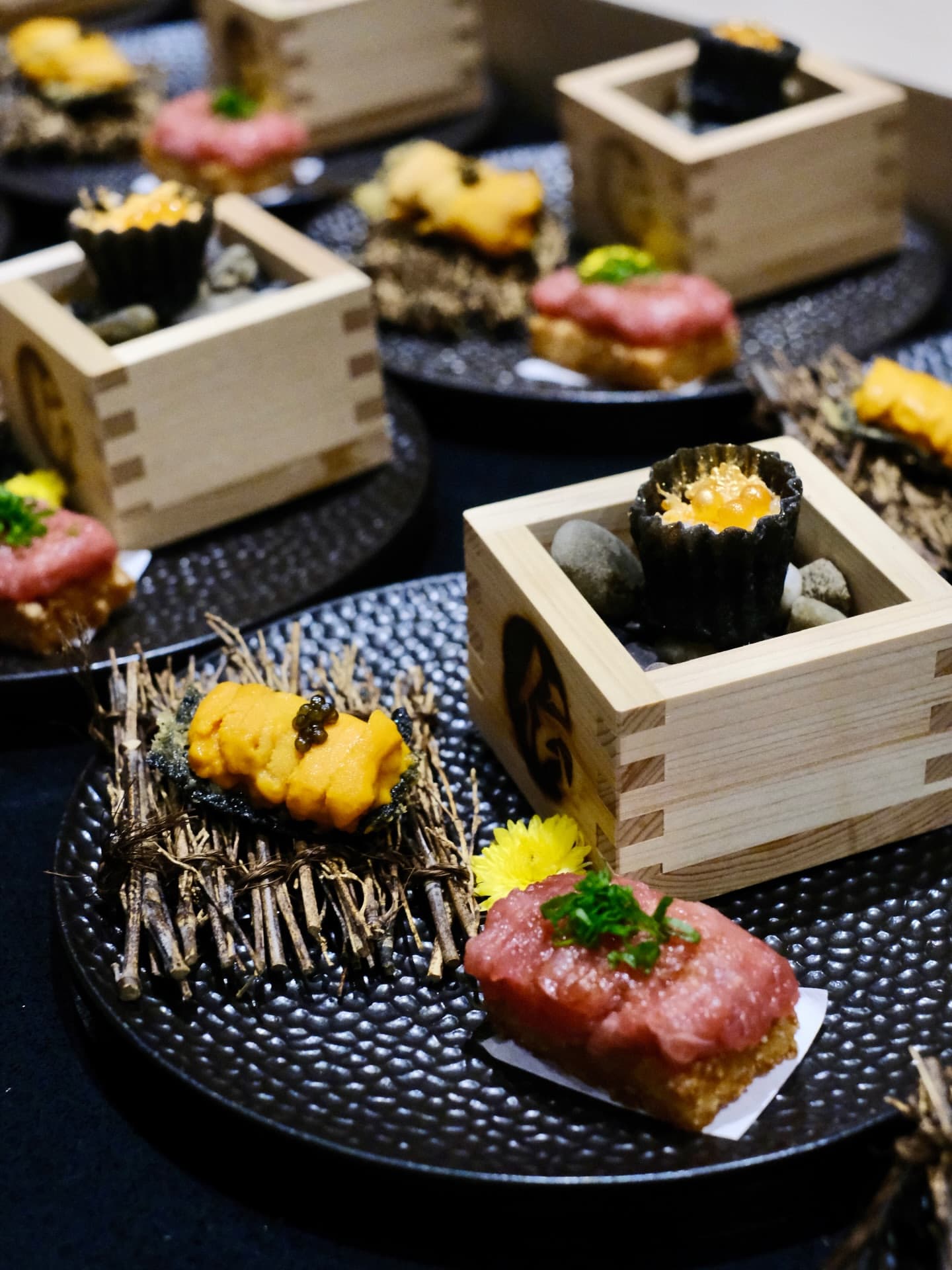 Tuna tartare bites and small dishes served in wooden masu cups on black plates